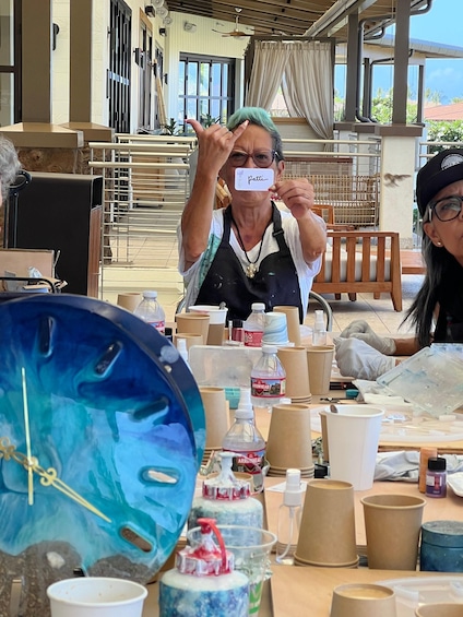 A person at a table with craft supplies, including paper cups, bottles, and a blue clock. 5