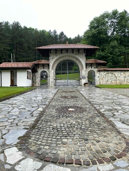 A stone pathway leading to a stone archway with a tiled roof, surrounded by greenery. 4