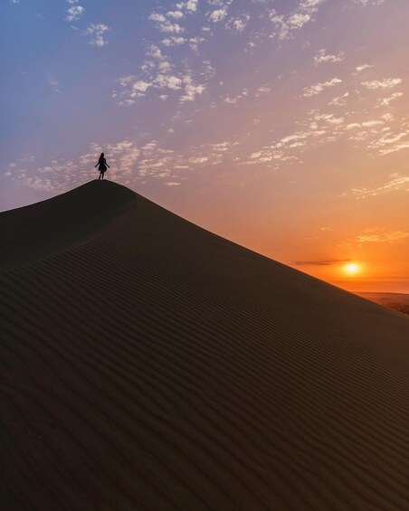 A person standing on a sand dune with a sunset in the background. 5