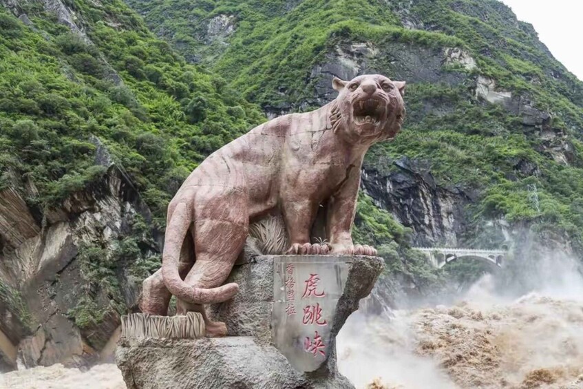 A stone statue of a tiger on a rock with a waterfall in the background. 2