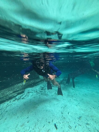 A diver underwater, holding a bottle, with a sandy ocean floor and another diver in the background. 1