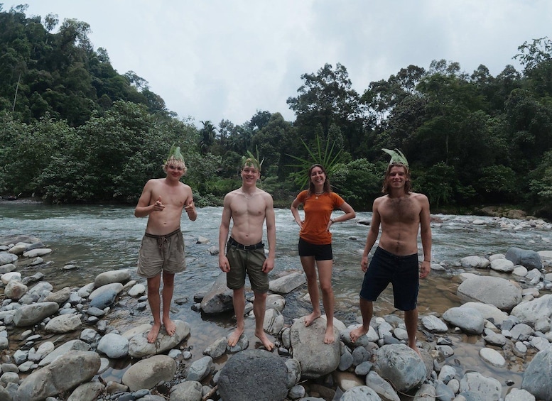 Four people standing on rocks by a river with trees in the background. 2