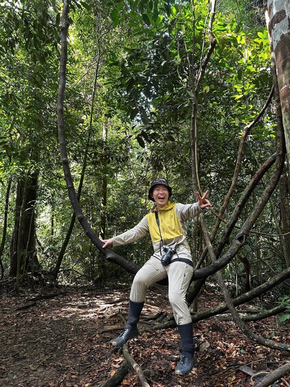 A person in a forest, wearing a yellow vest and black boots, sitting on a fallen tree branch. 5