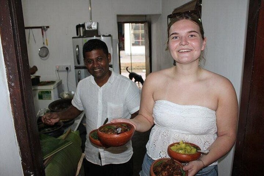 A person holding a bowl of food, another person in the background, and a kitchen area with appliances. 5