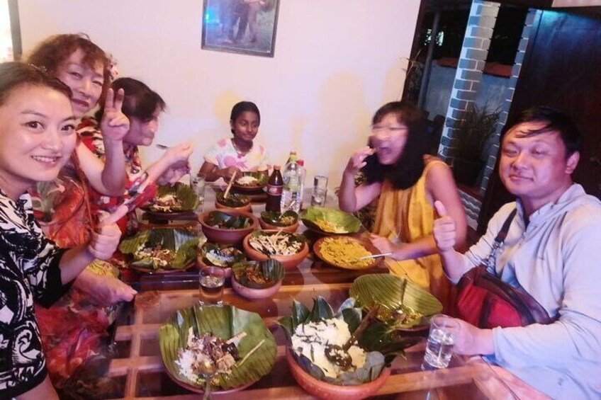 A group of people sitting around a table with food in banana leaves. 4