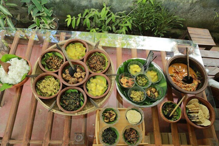 A variety of dishes served on a wooden table outdoors, surrounded by greenery. 1