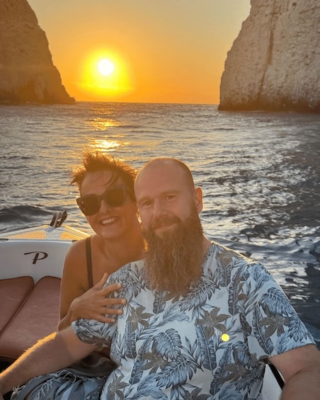Two people on a boat with a sunset and cliffs in the background. 5