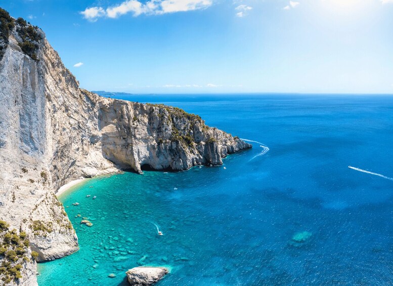 A coastal landscape with cliffs, clear turquoise waters, and a boat creating a wake. 3