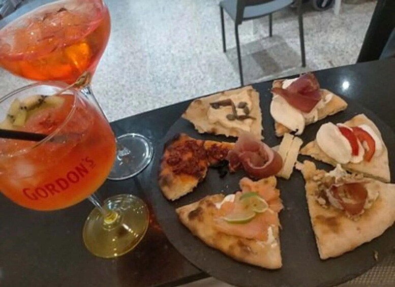 A table with a plate of pizza slices topped with various ingredients and two drinks, one of which is labeled 'GORDON'S'. 2