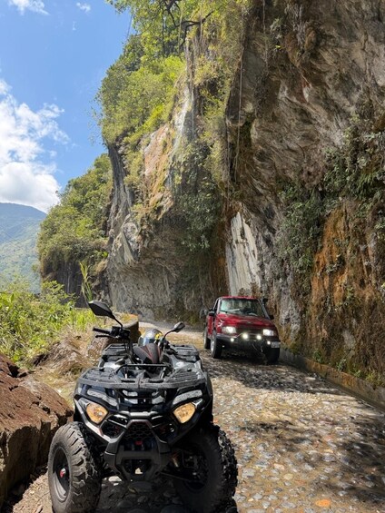 A rocky mountain road with a quad bike and a red car. 1