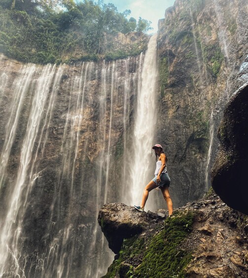 A person standing on a rock by a waterfall. 1