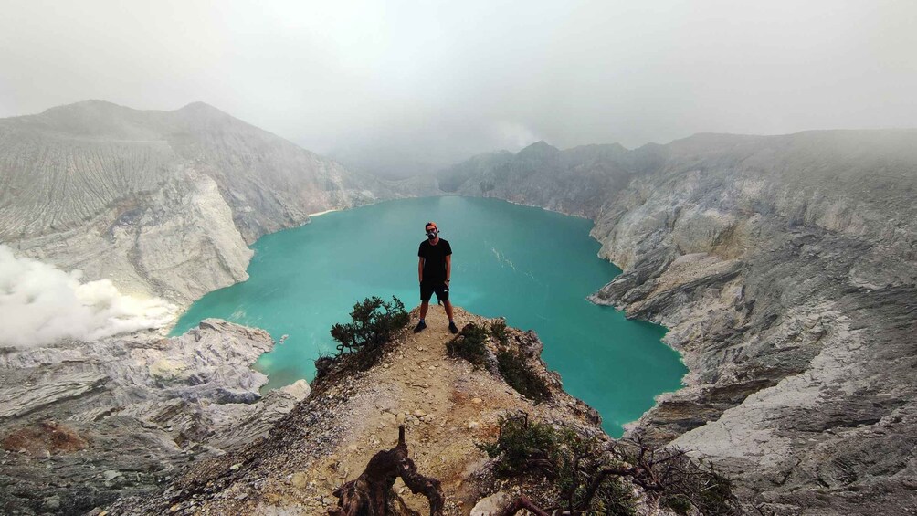 A person standing on a rocky ledge overlooking a turquoise lake surrounded by mountains. 3