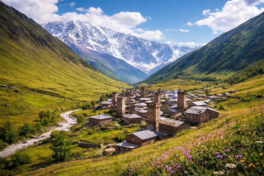 A village with stone buildings and a river, surrounded by mountains and fields. 1
