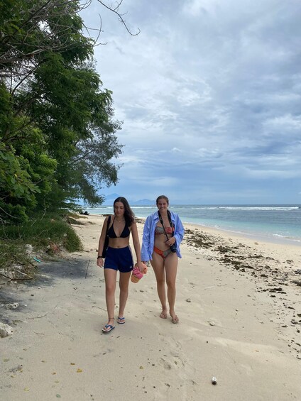 Two people walking on a sandy beach with ocean and mountains in the background. 2