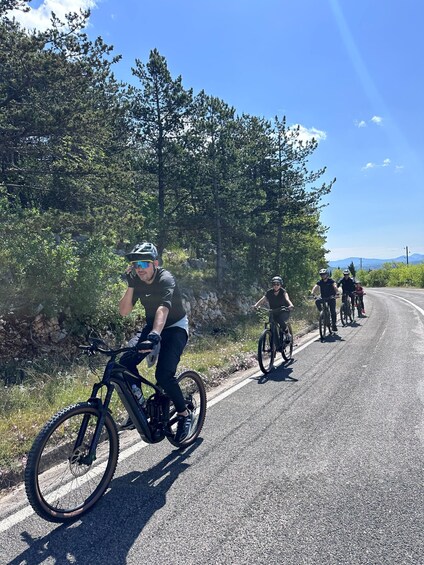 A group of cyclists on a paved road with trees and a clear sky in the background. 3
