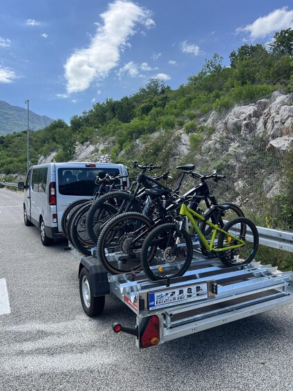 A silver van parked on the side of a road with a trailer carrying multiple bicycles. 4