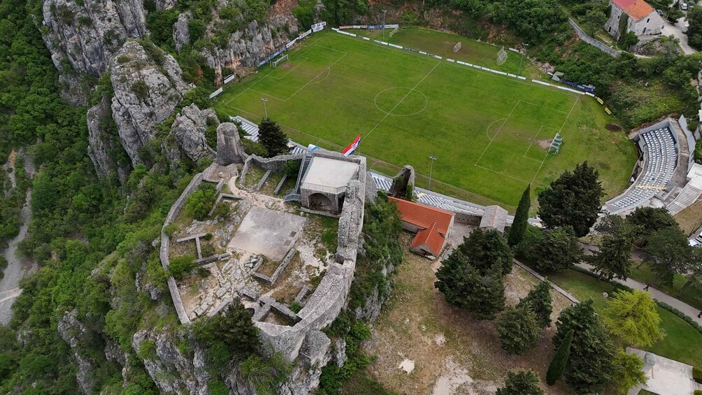 An ancient fortress with a soccer field, surrounded by rocky terrain and greenery. 2