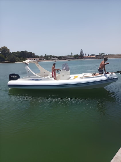 A small motorboat on calm water with two people on board, one steering and one standing. 4