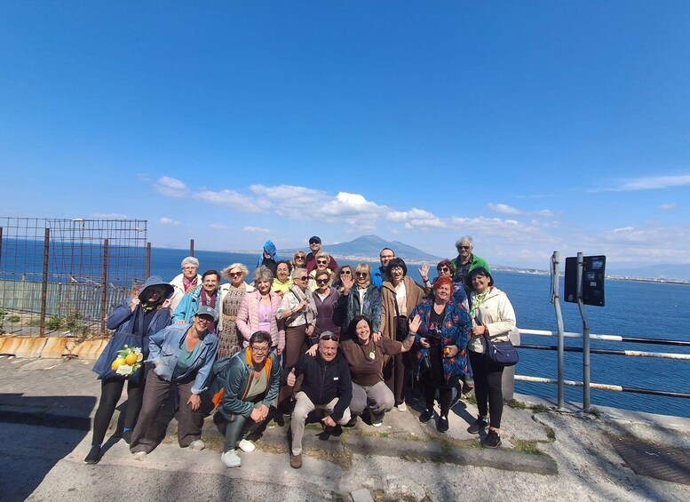 A group of people posing on a coastal walkway with a clear view of the sea and a distant mountain. 1