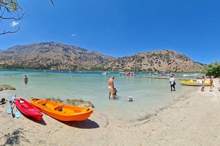 Una playa con kayak, gente nadando y montañas al fondo. 3