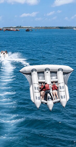 A group of people on a white inflatable boat with a jet ski creating a wake behind them. 1