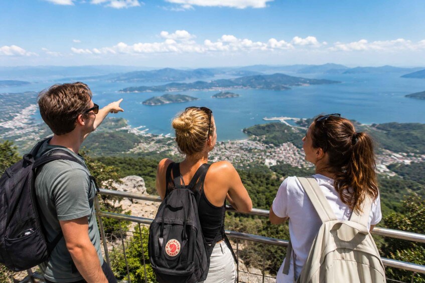 Three people overlooking a coastal landscape with mountains and a body of water. 3