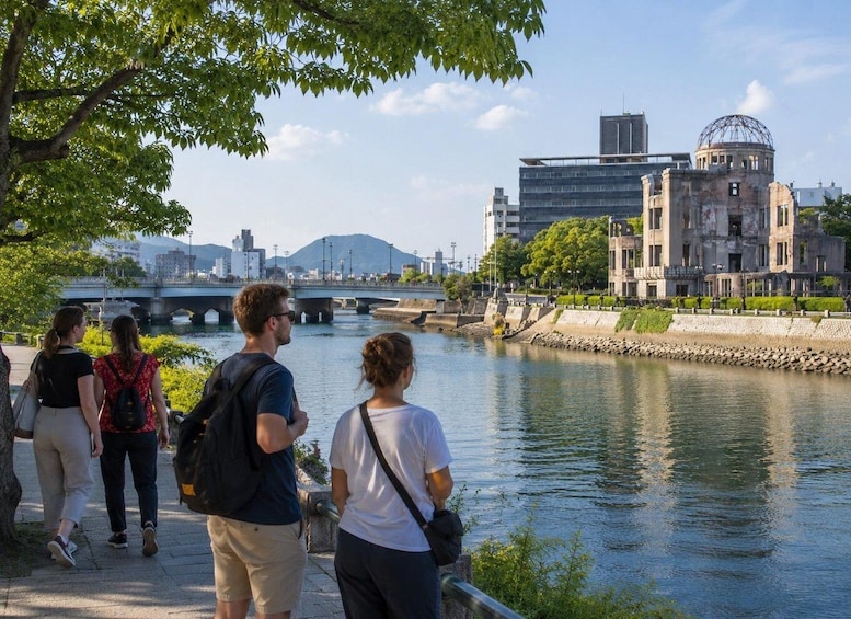 A group of people walking along a riverside path with a bridge and buildings in the background. 1
