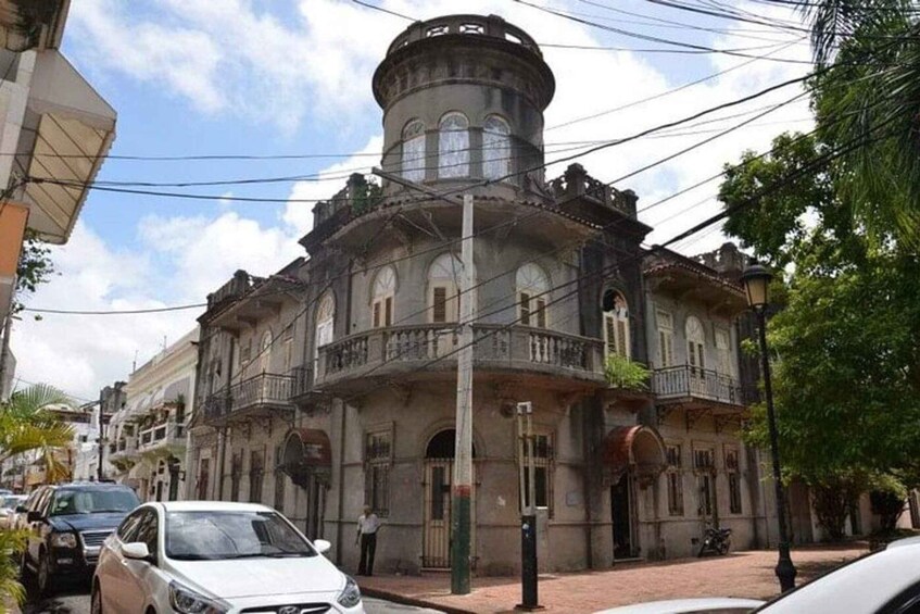 A historic building with a turret, a street with parked cars, and a pedestrian. 5