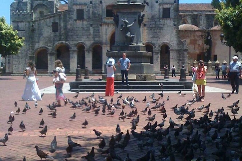 A historic building with a statue in front, surrounded by pigeons and people. 4