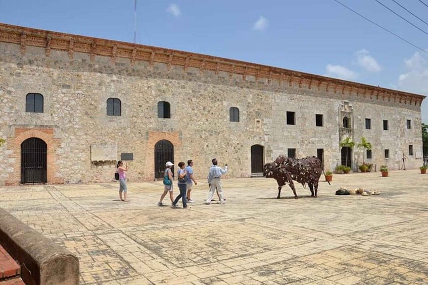 A historic stone building with arched doorways and a courtyard with a metal cow sculpture. 2