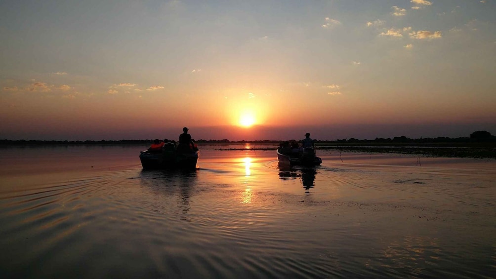 Two boats on a calm body of water with a sunset in the background. 1