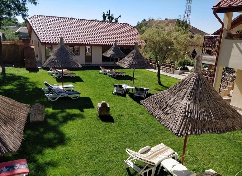 A well-maintained lawn with sun loungers and thatched umbrellas, a building with a tiled roof, and a clear sky. 5