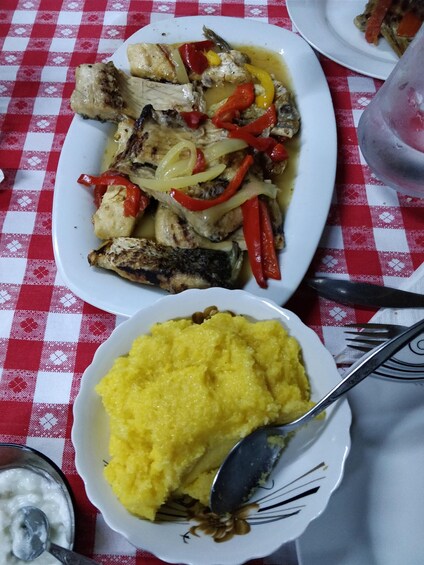 A plate of grilled fish with bell peppers and a bowl of yellow polenta. 4