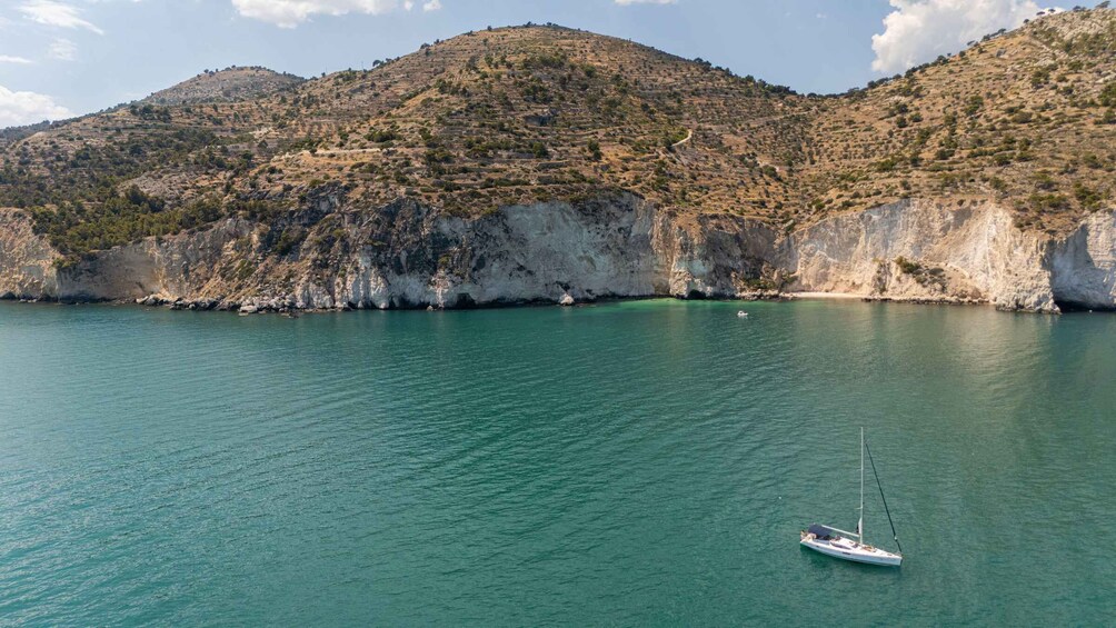 A calm sea with a sailboat anchored near a rocky coastline. 1