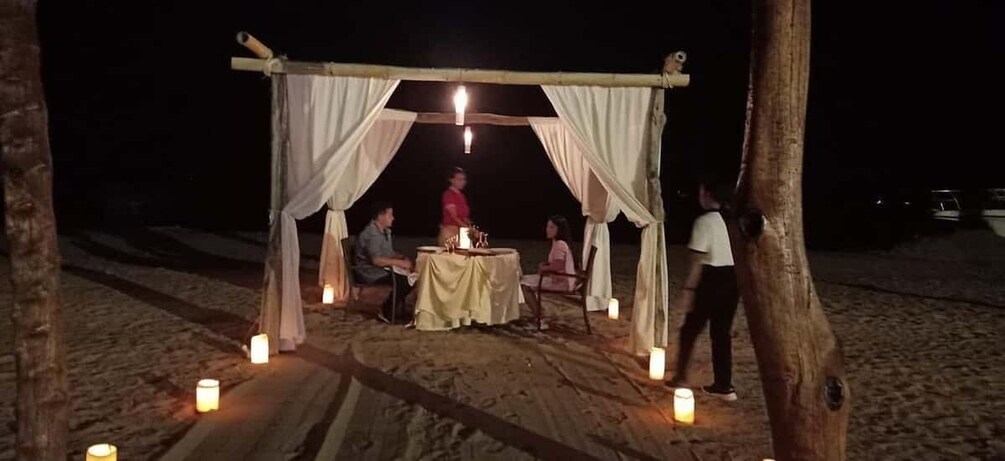 A tented dining area with candles on the sand. 1