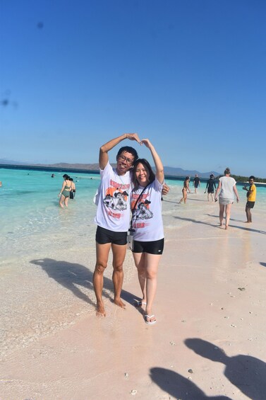 Two people on a beach with clear turquoise water and distant mountains. 3
