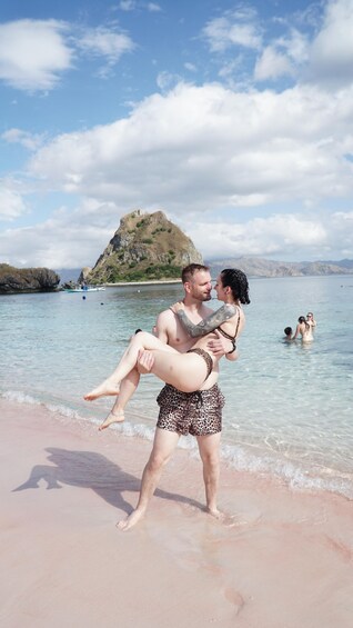 A couple on a beach with clear water and a rocky island in the background. 4