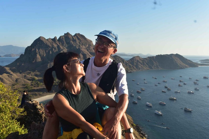 A couple sitting on a cliff overlooking a bay with numerous boats. 5