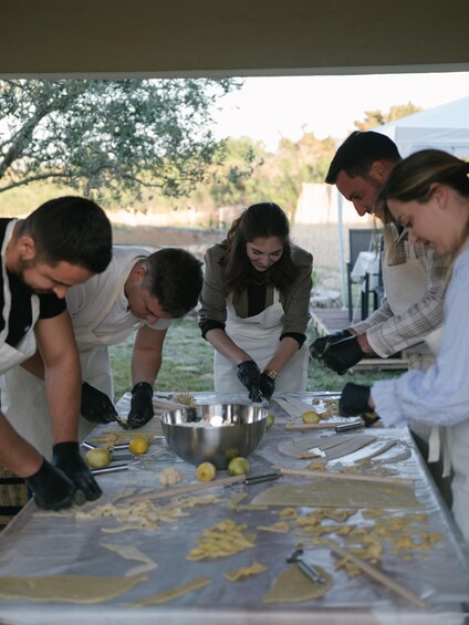 People preparing food outdoors with a table covered in ingredients and utensils. 1