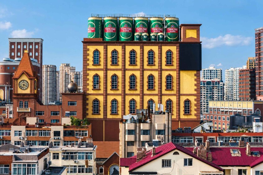 A cityscape with a yellow building topped with green and red cans, surrounded by modern high-rises. 1