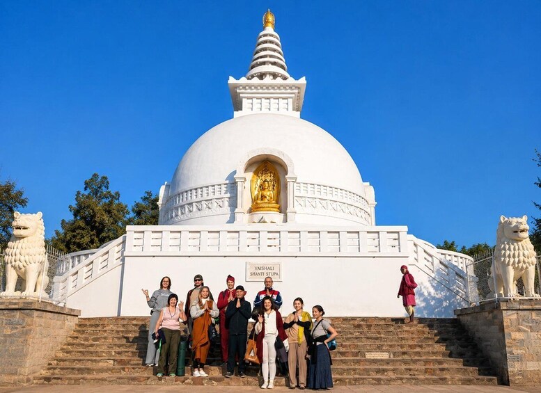 En hvid stupa med en gylden statue, omgivet af stenen løvefigurer, og en gruppe mennesker foran. 5