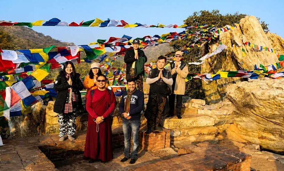 A group of people standing on stone steps with colorful prayer flags in the background. 3