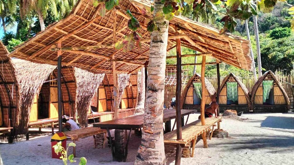 Thatched-roof huts with wooden benches and tables, surrounded by palm trees and a sandy beach. 3