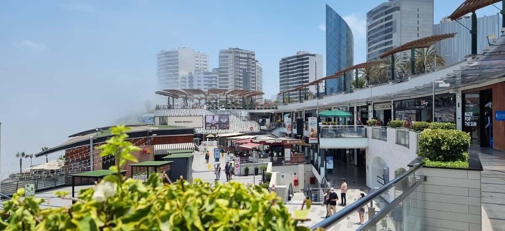 A bustling urban plaza with modern buildings, outdoor seating areas, and a clear view of the waterfront. 5