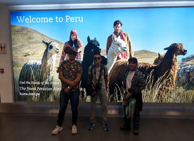 A group of people standing in front of a large welcome sign for Peru, featuring llamas and a mountainous landscape. 2