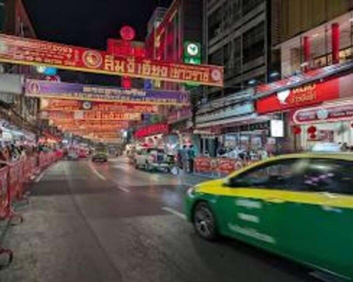 A busy street at night with illuminated signs and a green taxi. 5