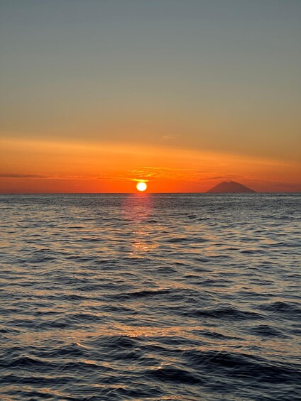 A sunset over the ocean with a mountain silhouette in the distance. 2