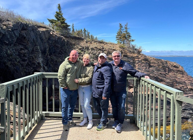 A group of people standing on a wooden staircase with a rocky cliff and ocean in the background. 1