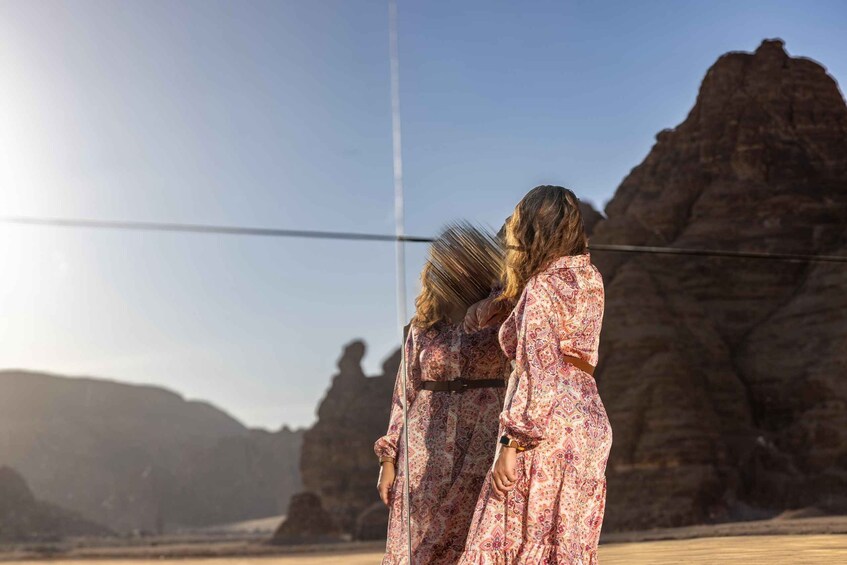 Two people in a patterned dress standing in a desert with rock formations in the background. 1