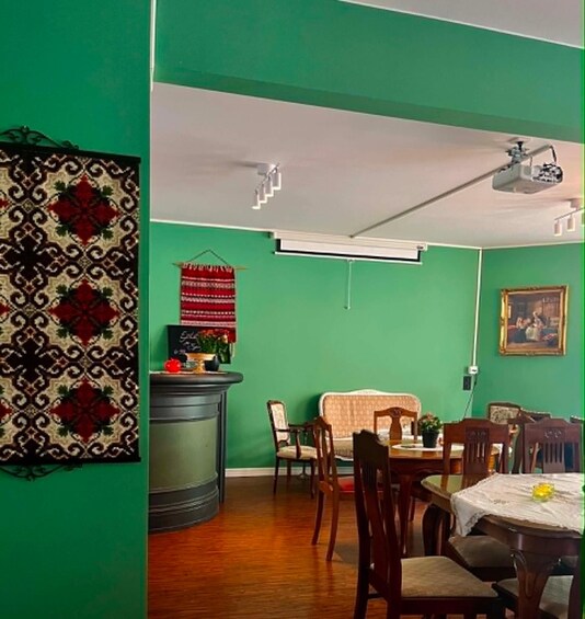 A dining area with a green wall, a patterned rug, a table with chairs, a ceiling fan, and a framed picture. 2